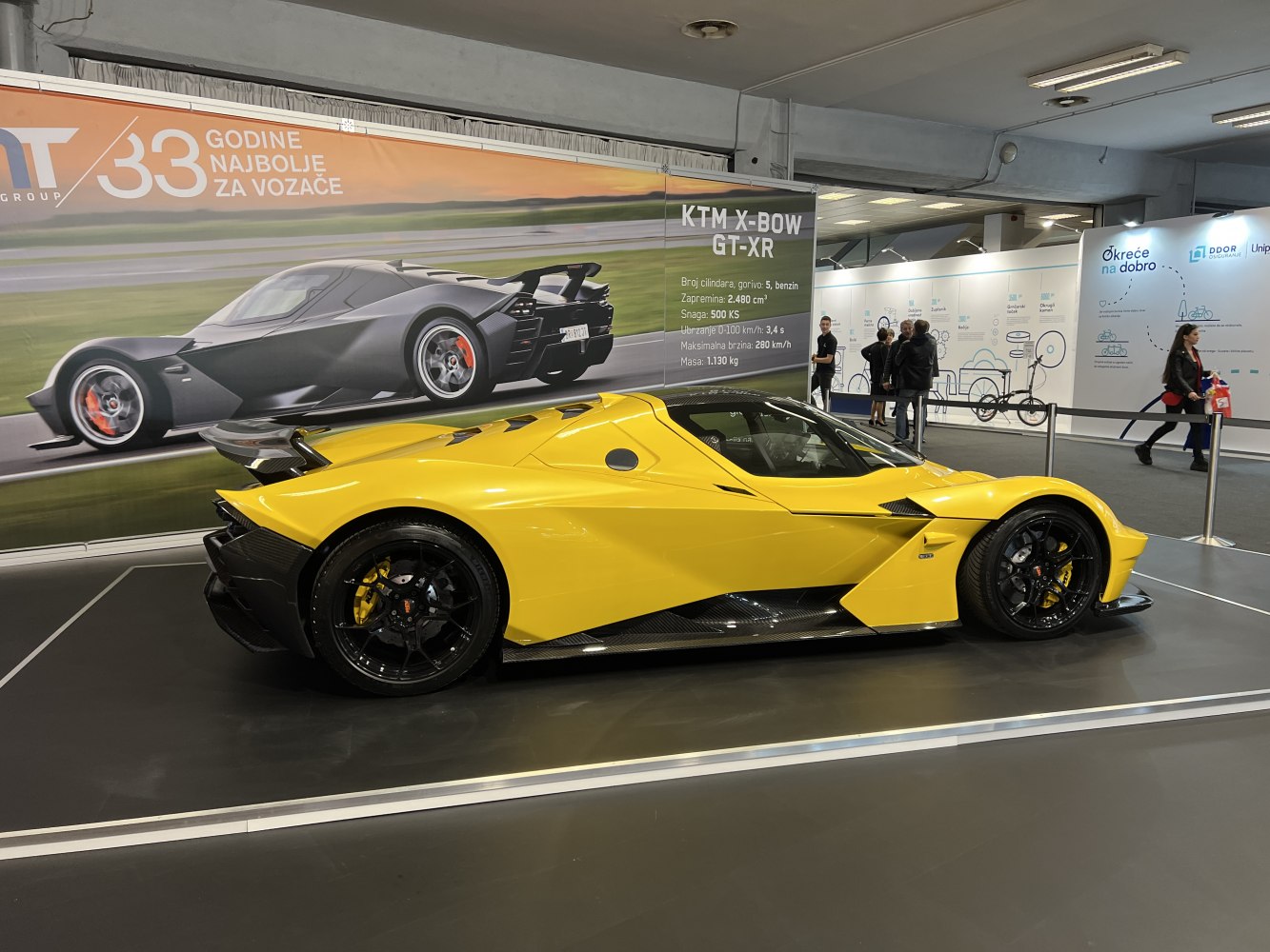 Yellow aerodynamic sports coupe with black carbon fiber details displayed indoors
