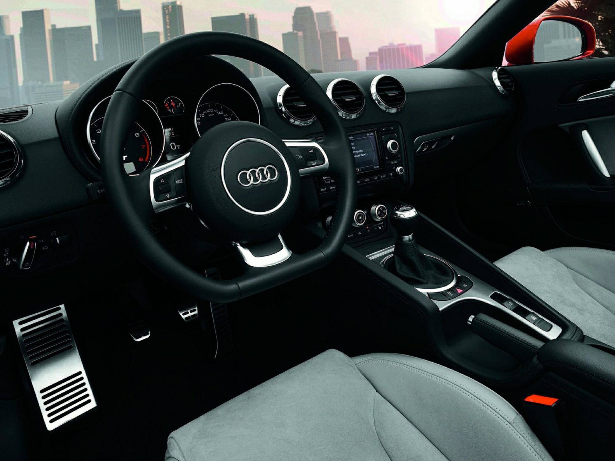 Audi sports car interior with steering wheel, gauge cluster, manual gear shift, pedals, and dashboard air vents