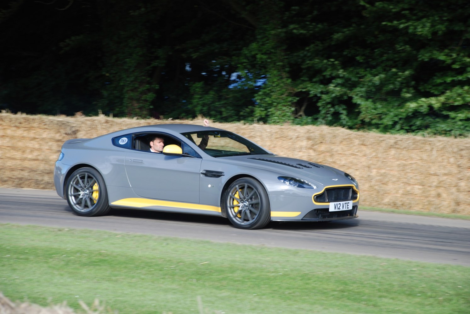 Grey sports coupe with yellow trim and vented hood racing on track