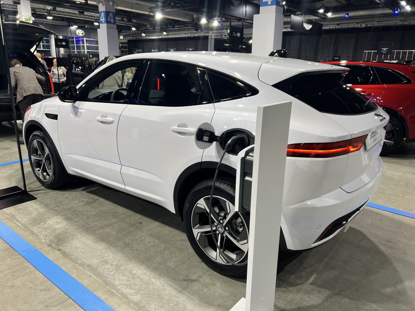 White electric SUV charging at an indoor station with alloy wheels and rear light design