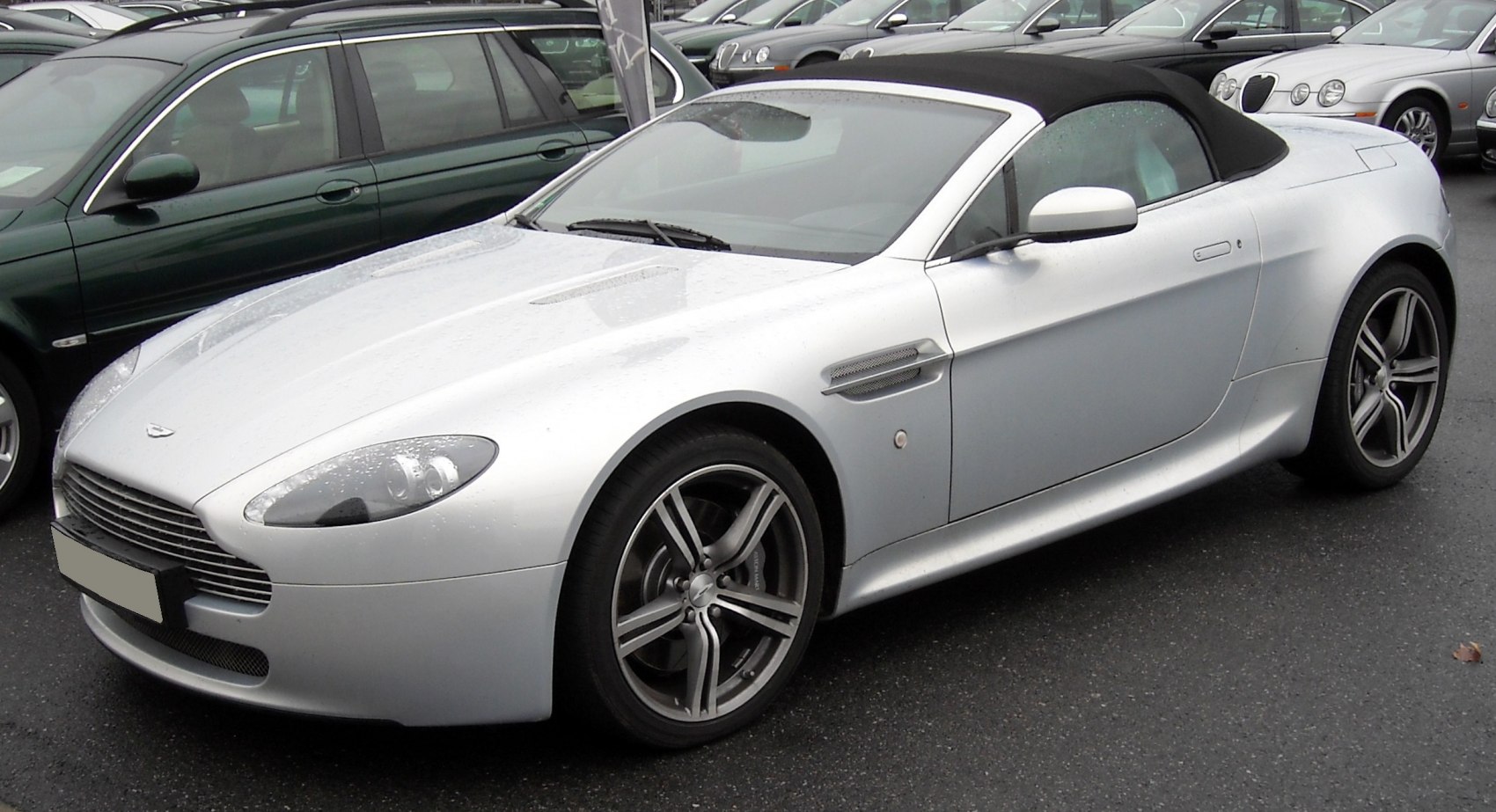 Silver convertible with black soft-top and sporty rims, front side view.