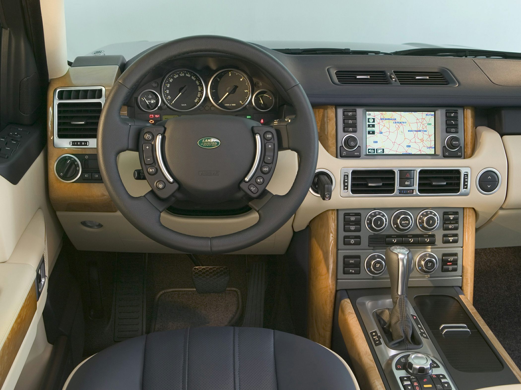 Steering wheel with controls, navigation display, wood trim, and climate control panel in luxury SUV interior