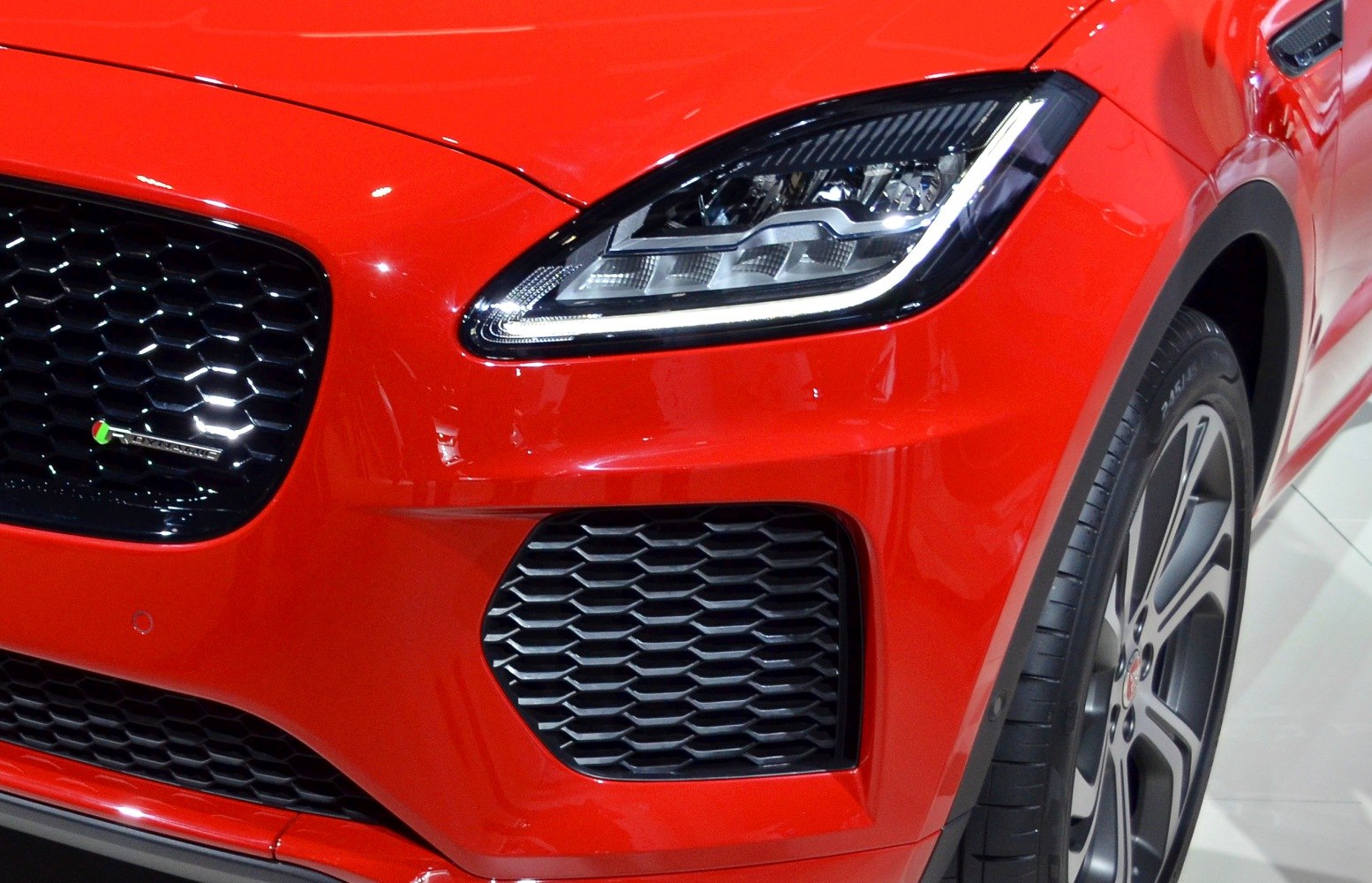 Detailed front headlight, grille, and wheel of a red sporty SUV.