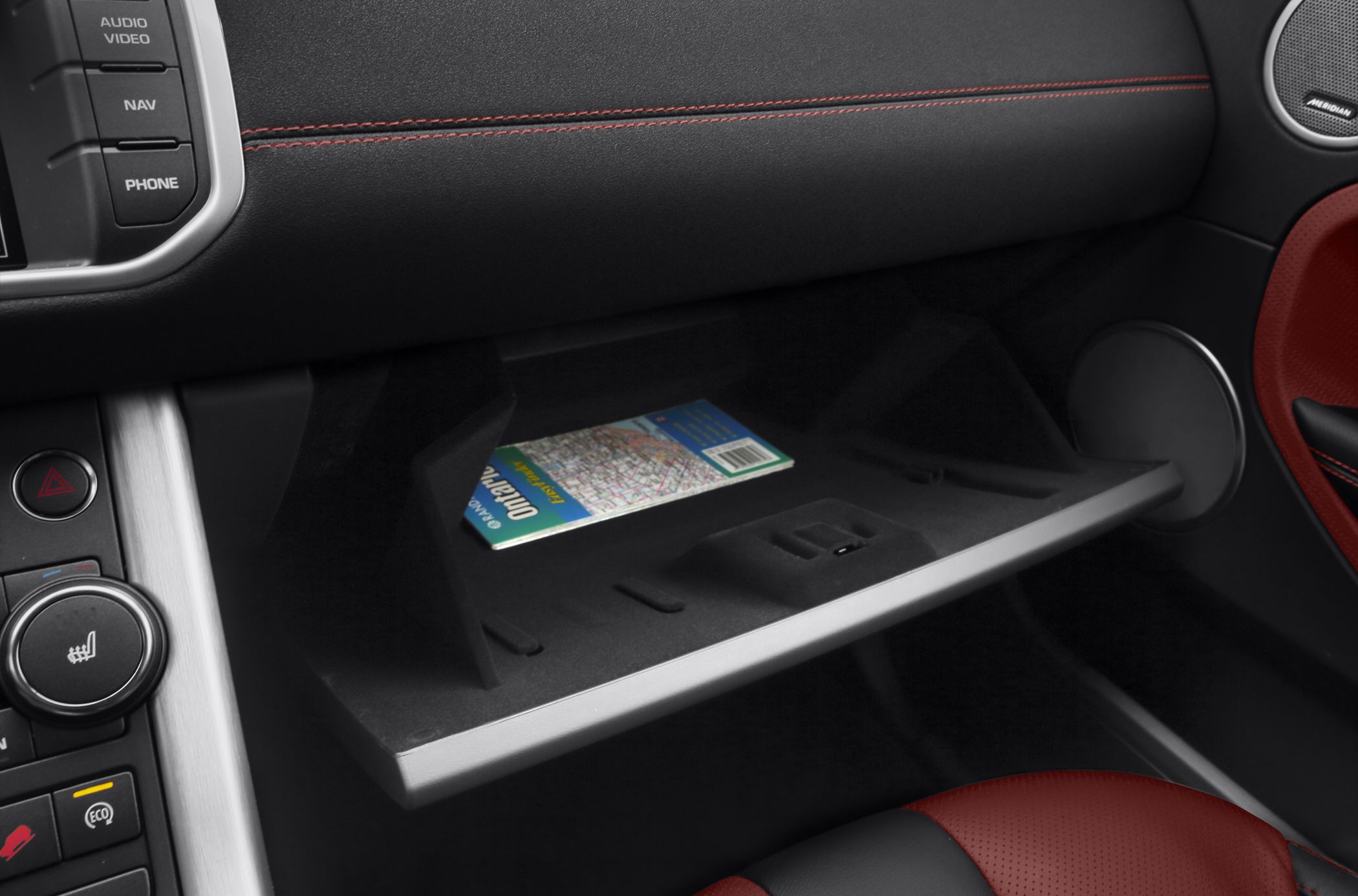 Open glove compartment with a map inside and part of the dashboard with controls.