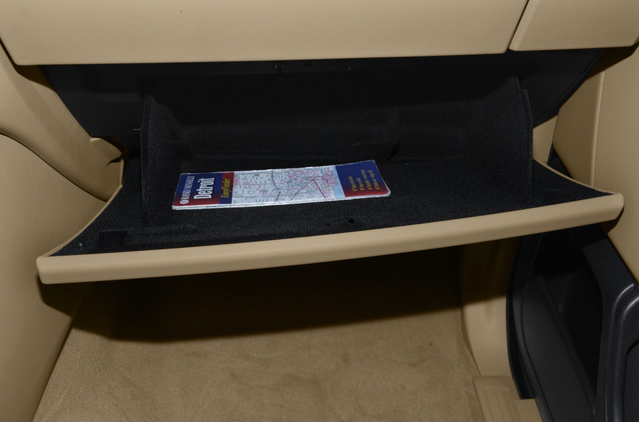 Beige glove box storage compartment with a folded map inside.
