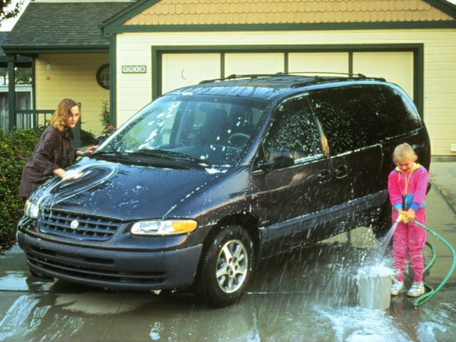 Black minivan hand washed in driveway by two people.