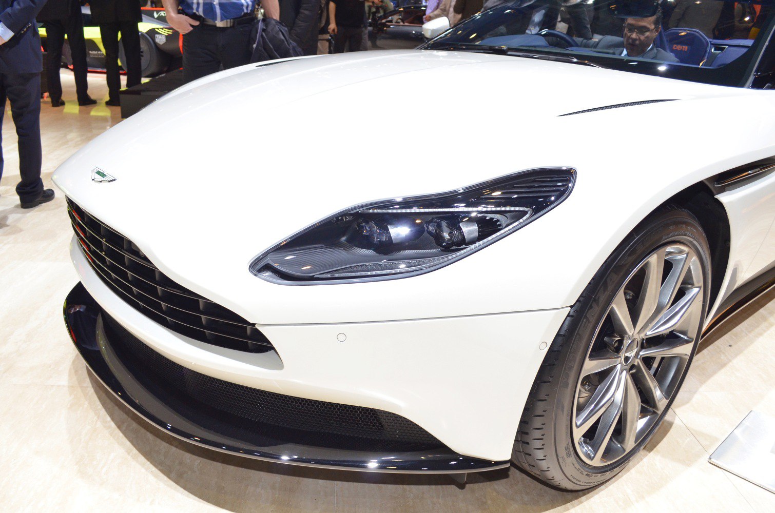 Close-up of front headlight, grille, and alloy wheel on white convertible