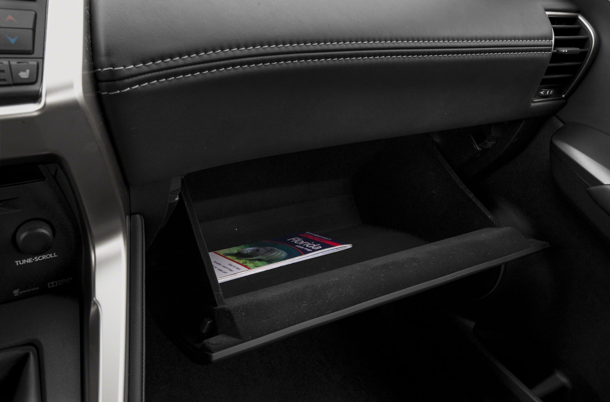 Open glove compartment with leather dashboard stitching and travel brochure