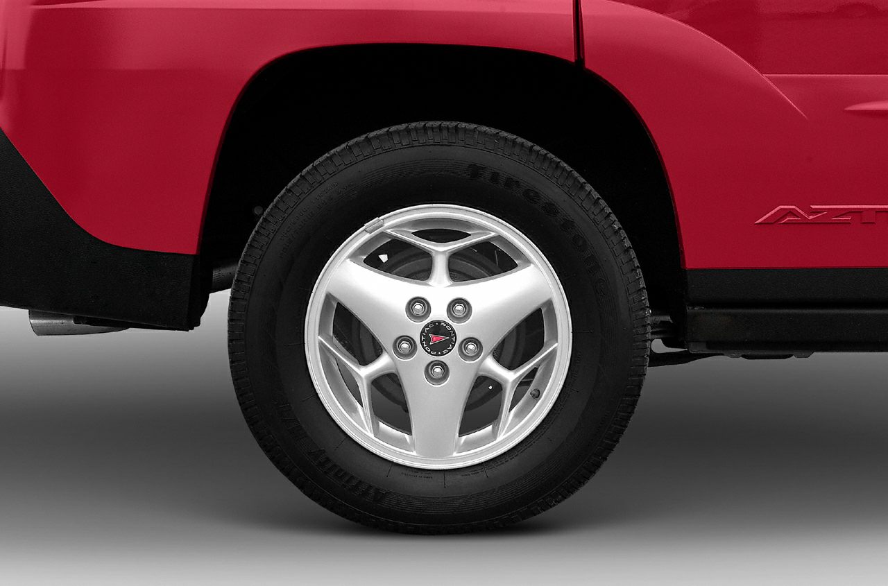 Silver alloy wheel and tire close-up on red body panel with Aztec badge