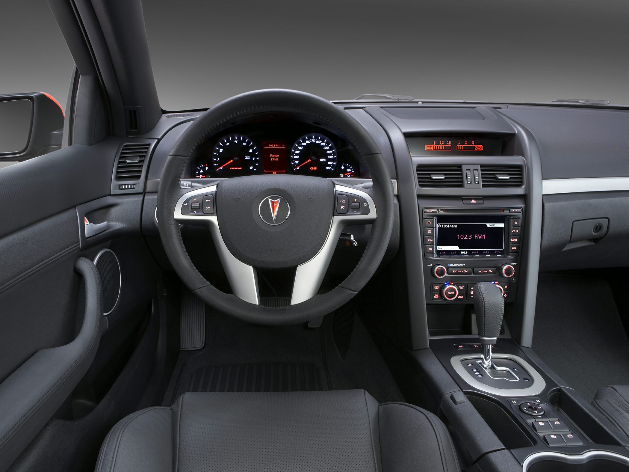 Steering wheel and center console with dashboard gauges and gear shift.