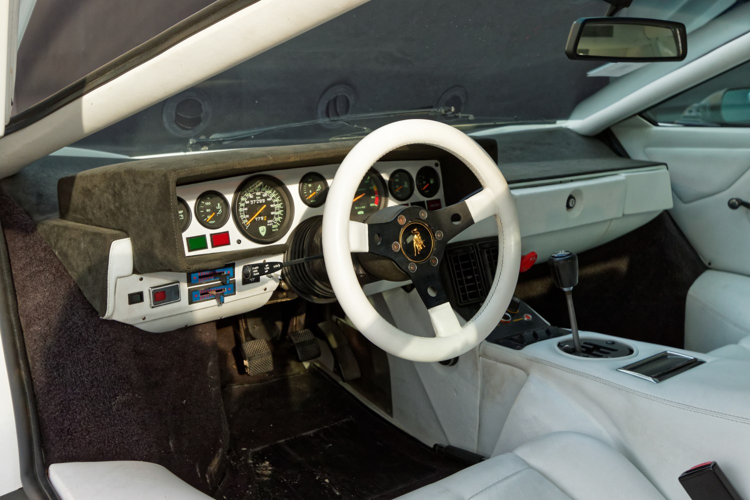 Vintage white steering wheel and analog dashboard gauges with manual gear lever and pedals.