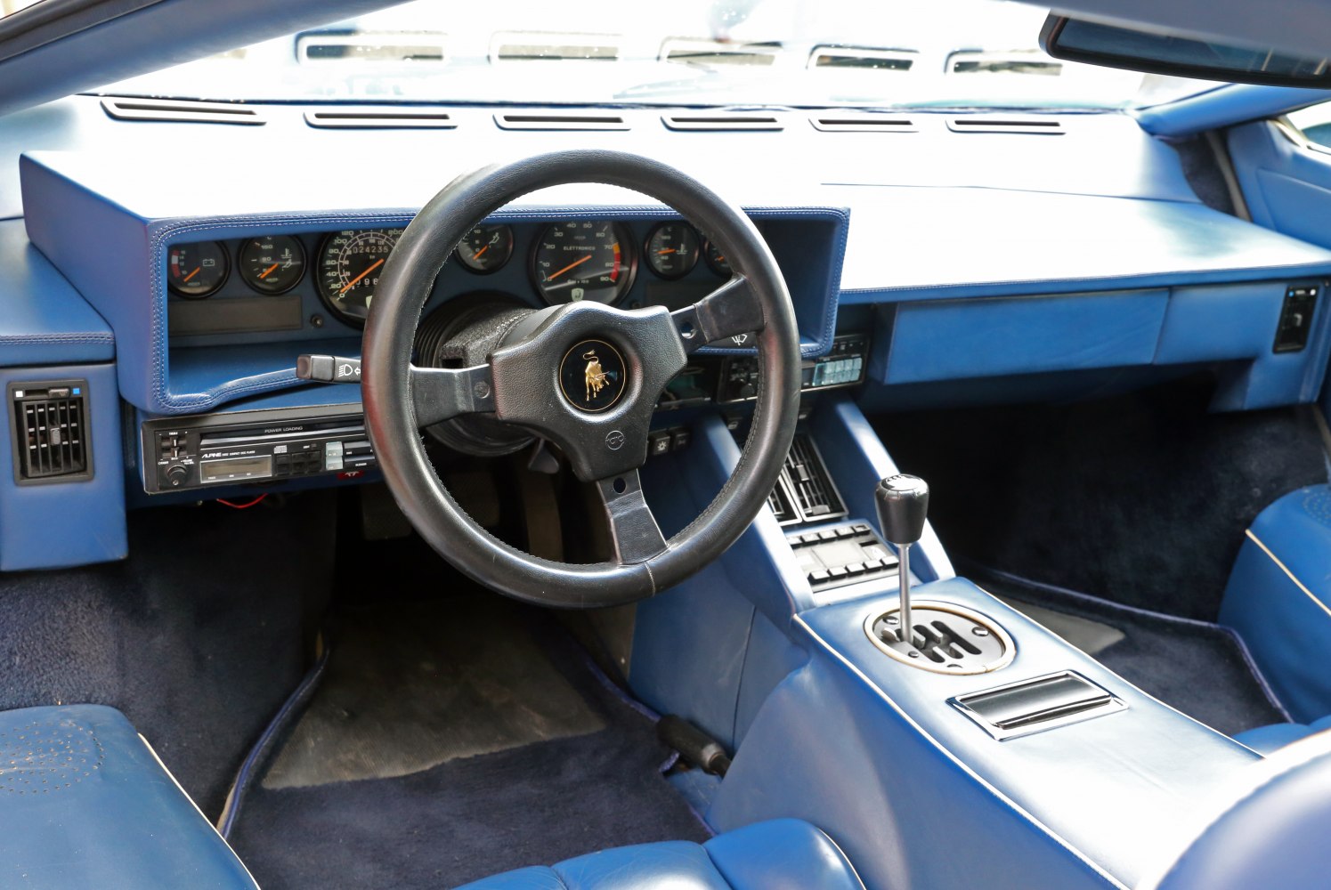 Manual gearshift, black steering wheel with emblem, blue leather interior