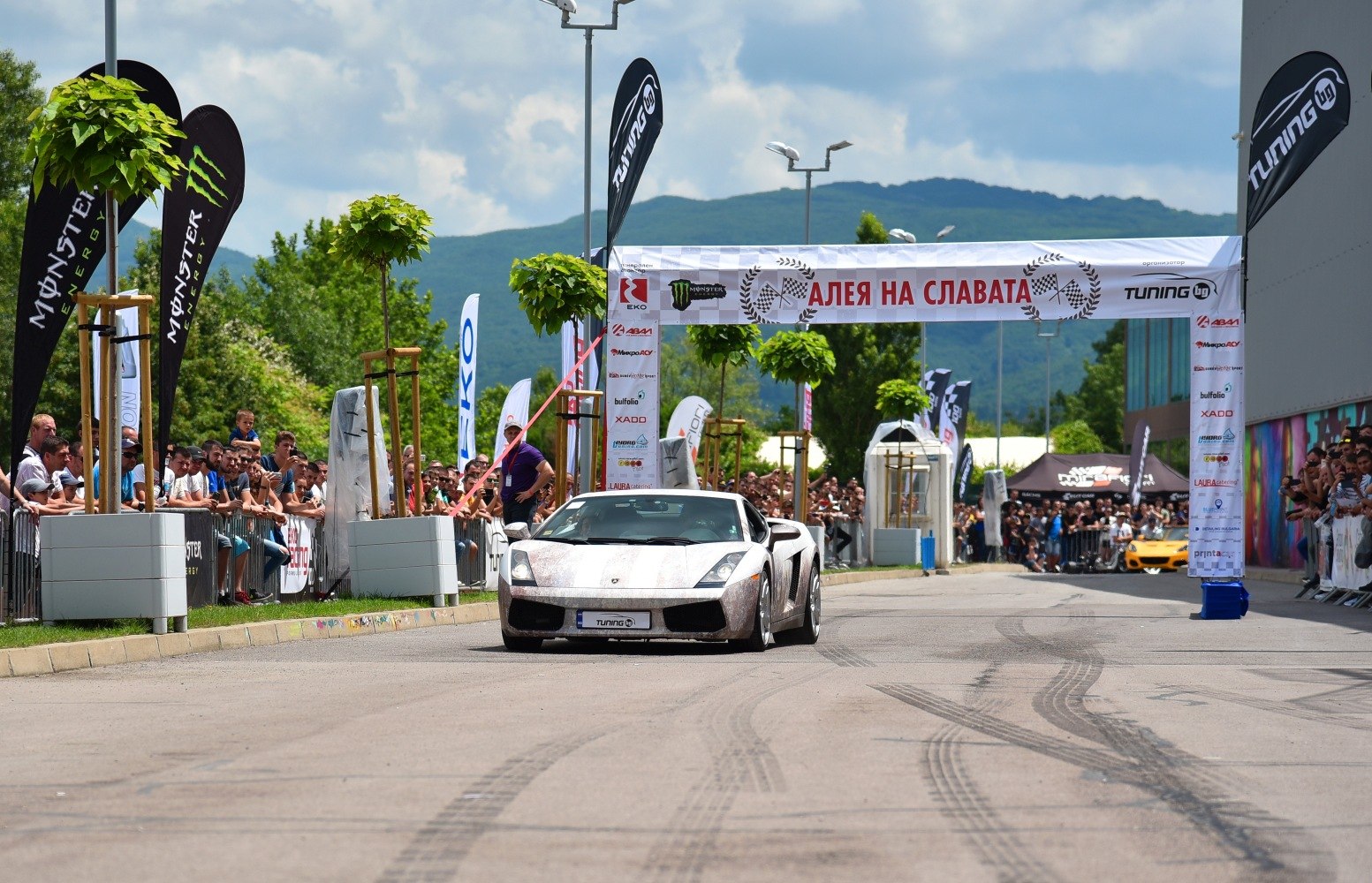 Front view of a sports car crossing event start line with crowd and banners