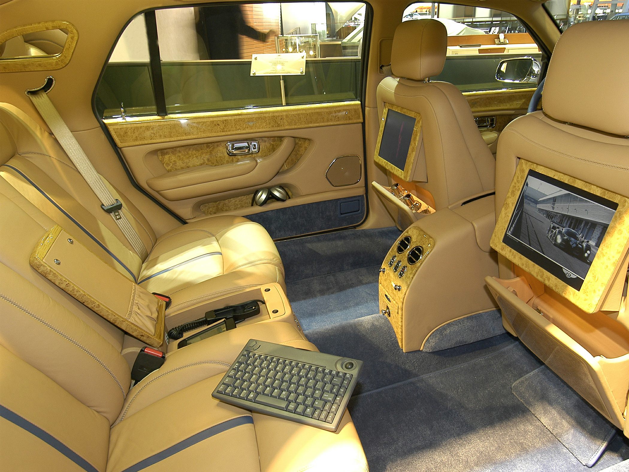 Luxurious rear cabin with dual screens, leather seats, wood trim, and a detachable keyboard.