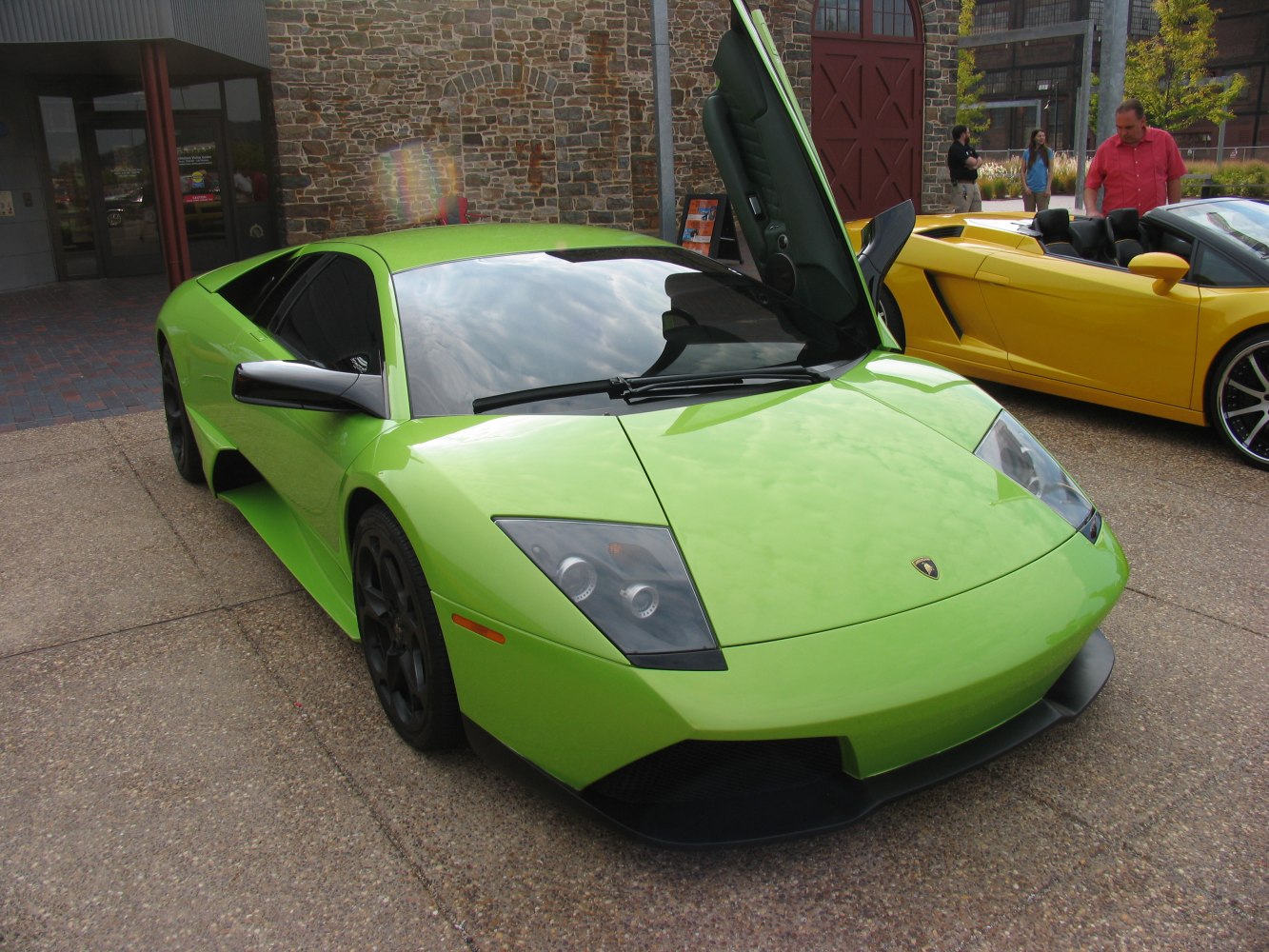 Front of sports car with vertical (scissor) door open, sleek headlights, and side mirror