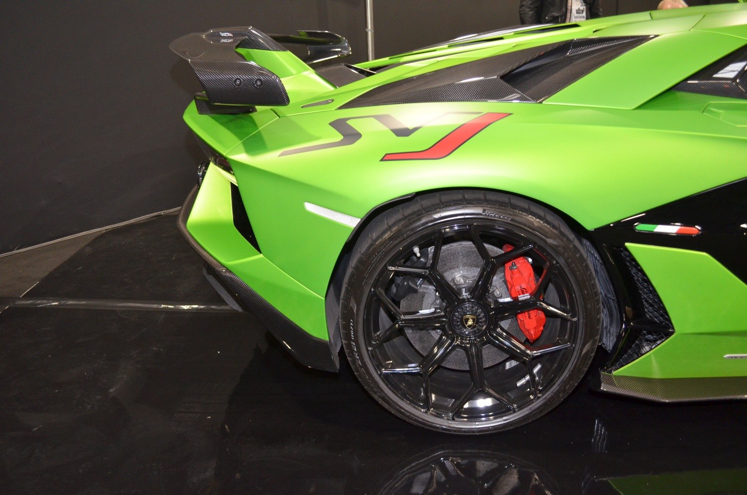 Rear wheel with black alloy rim, red brake caliper, and large carbon fiber aerodynamic wing.