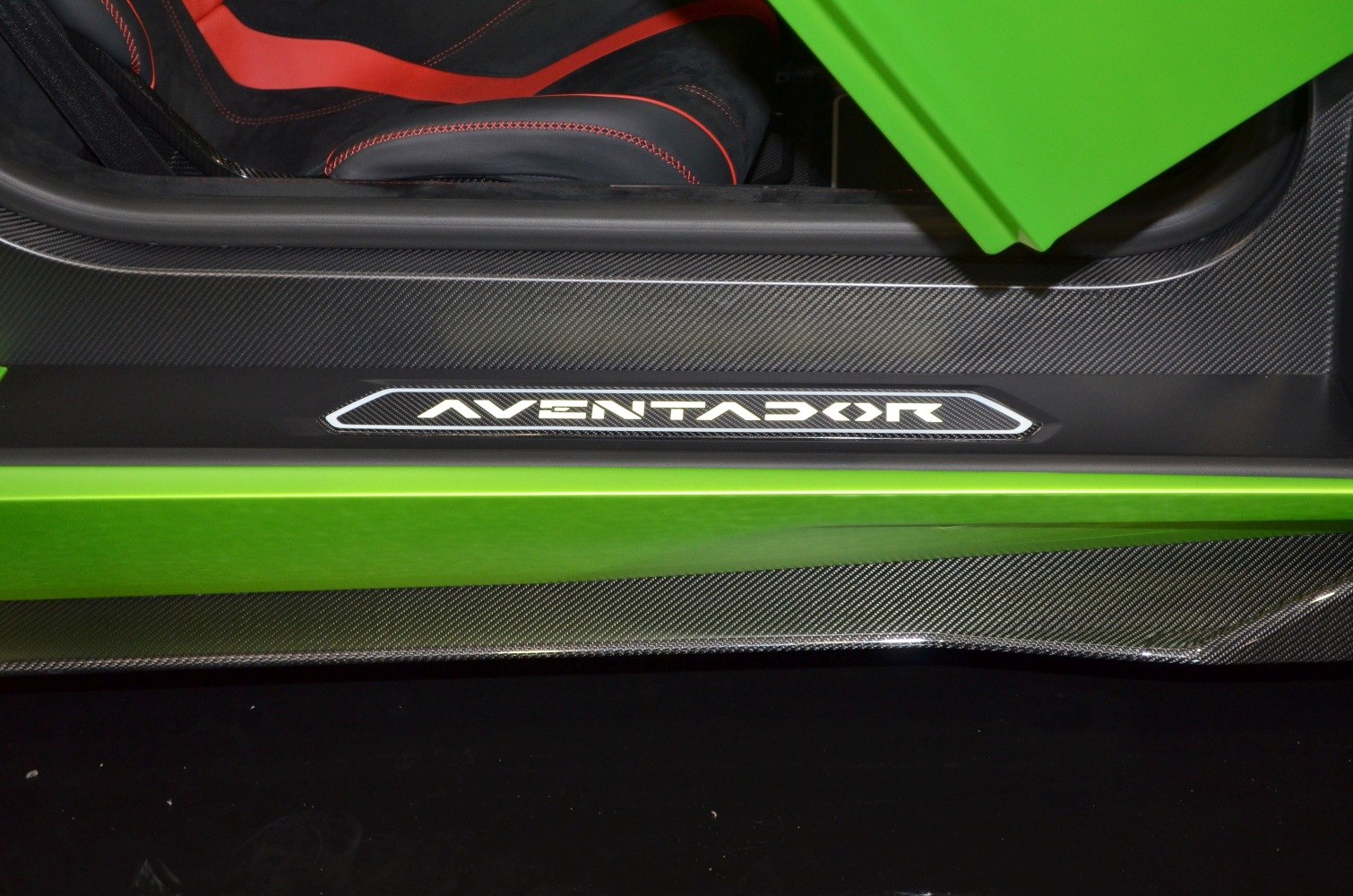 Carbon fiber door sill with illuminated Aventador logo and red-trimmed black seat