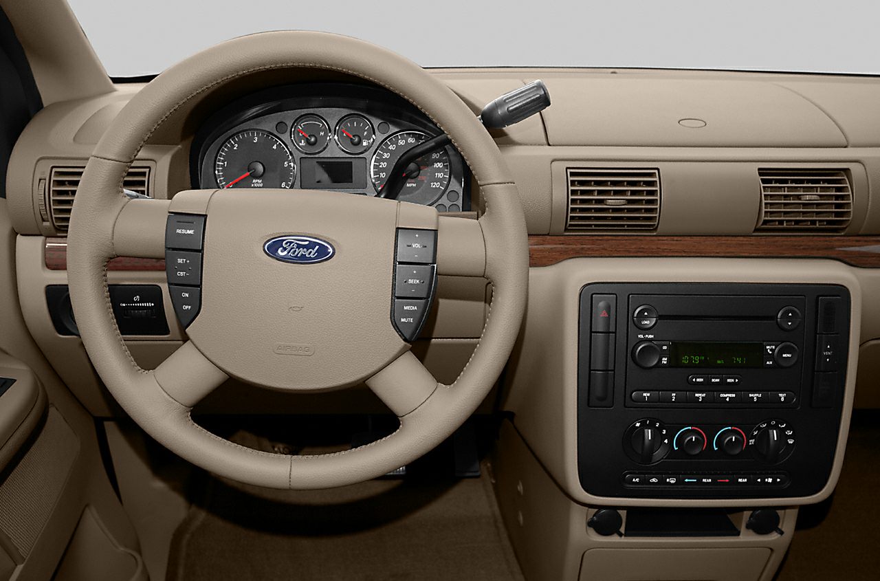 Beige steering wheel and dashboard with wood trim and control buttons.