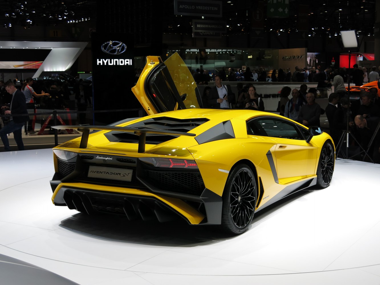 Yellow sports car rear with open vertical scissor door and aerodynamic wing