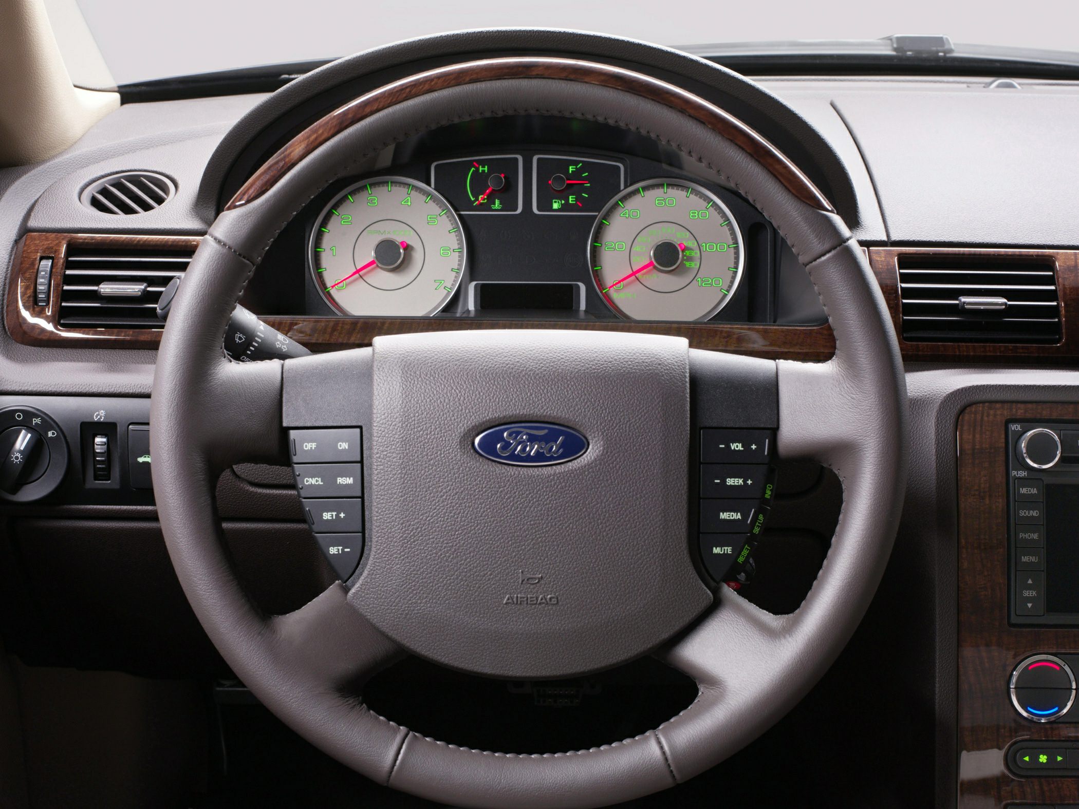 Steering wheel with controls and instrument cluster with gauges and wood trim.