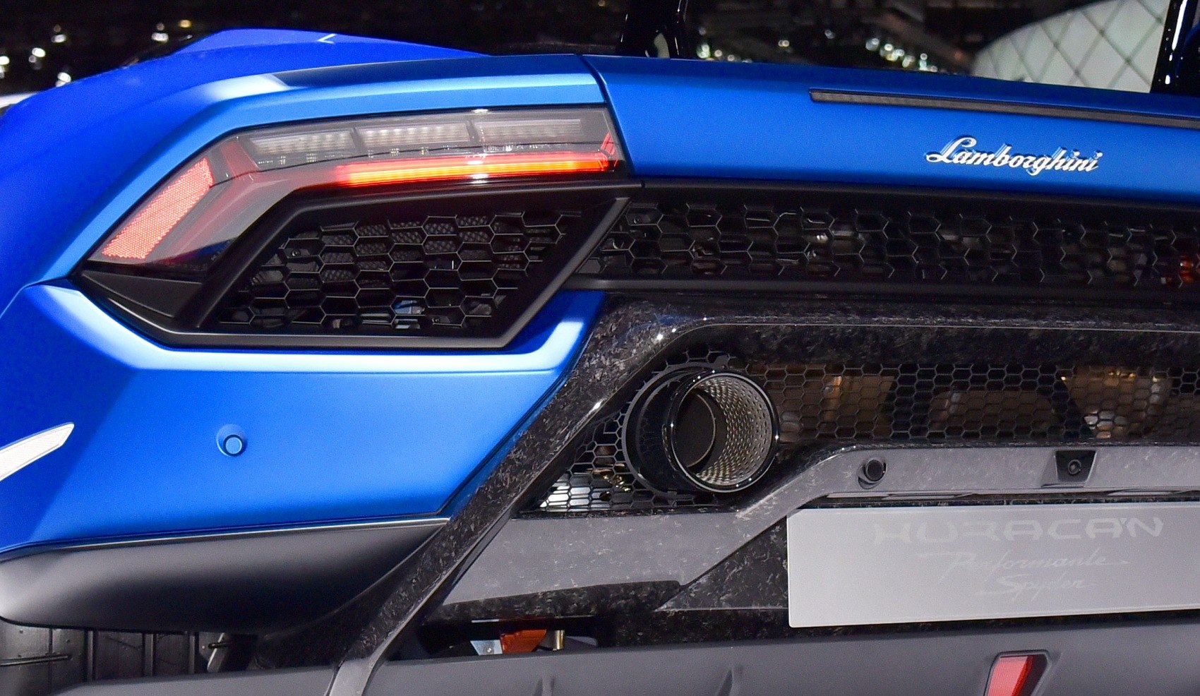 Rear exhaust and taillight with hex grille on blue sports car.