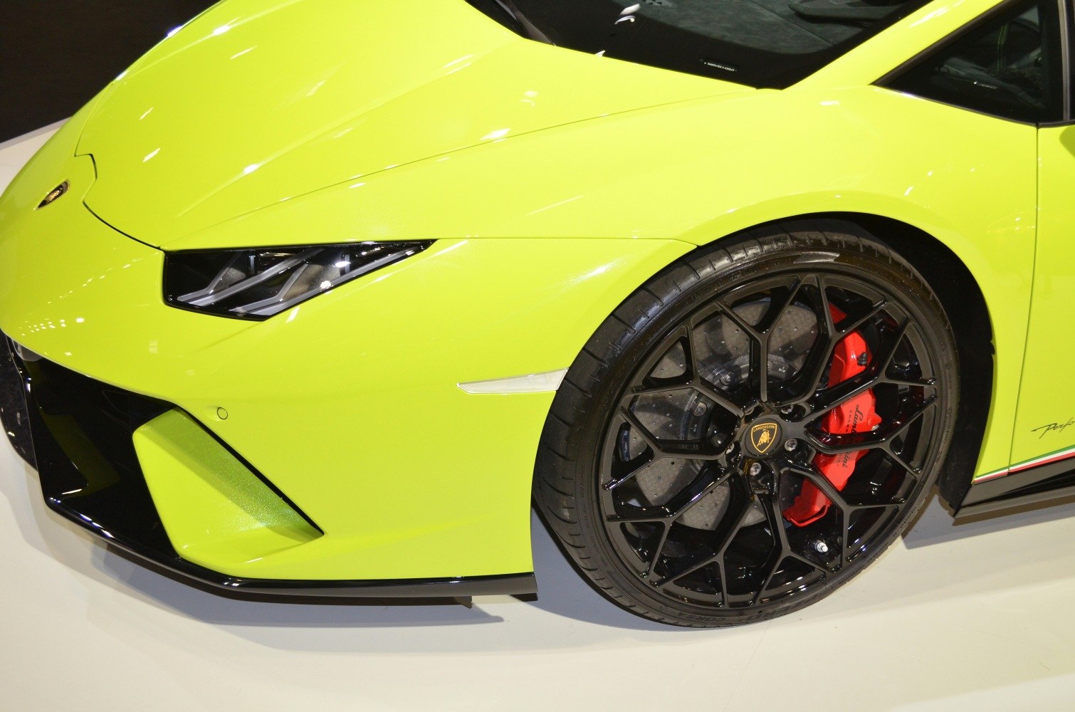 Front wheel with black alloy rim and red brake caliper, angular headlight