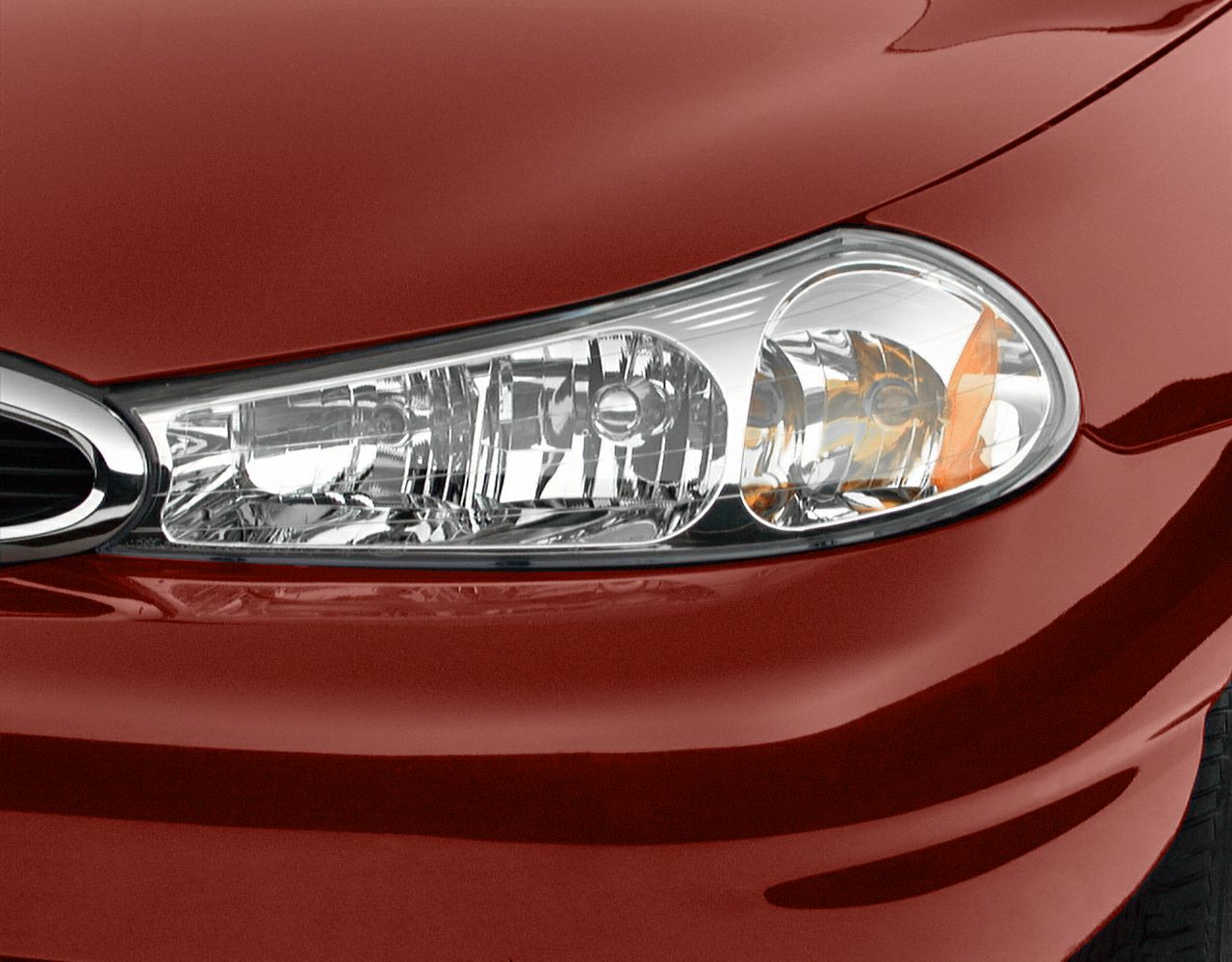 Close-up of a clear lens headlight with amber reflector on red paint.