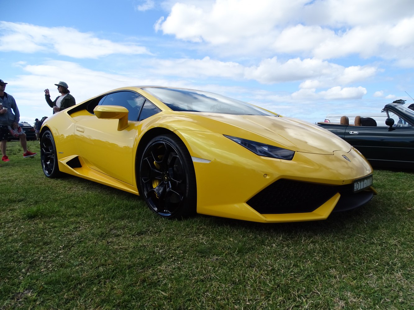 Yellow supercar with sharp front end and black wheels on grass
