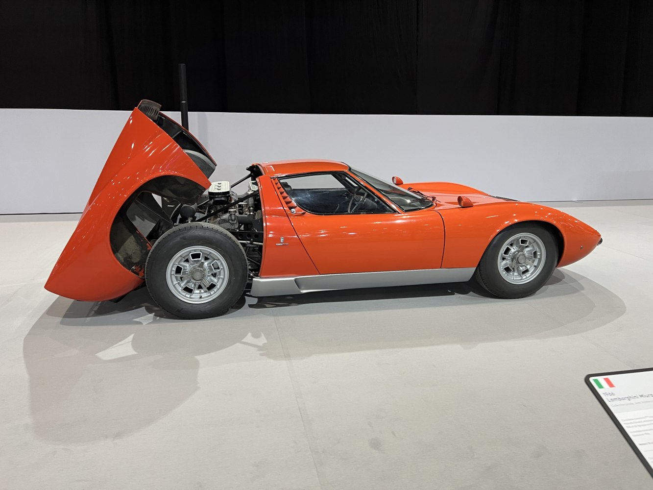 Side view of mid-engine sports car with rear hood open and vintage wheels.