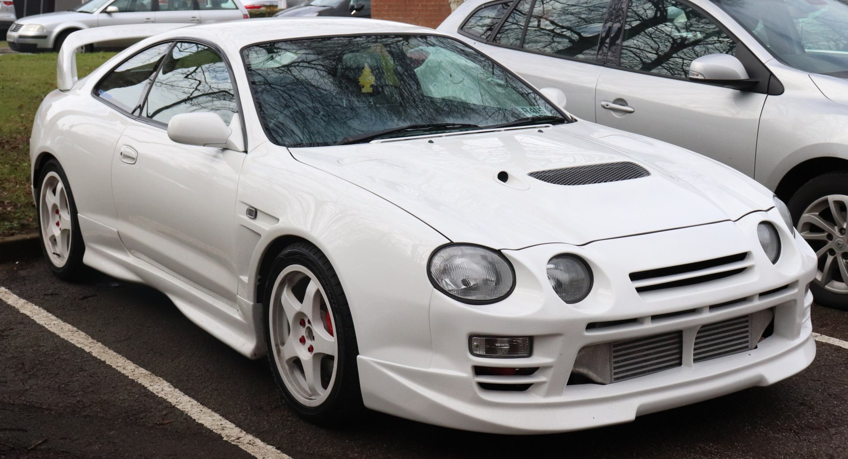 Dual round headlights, hood scoop, wide body kit, white sporty wheels.