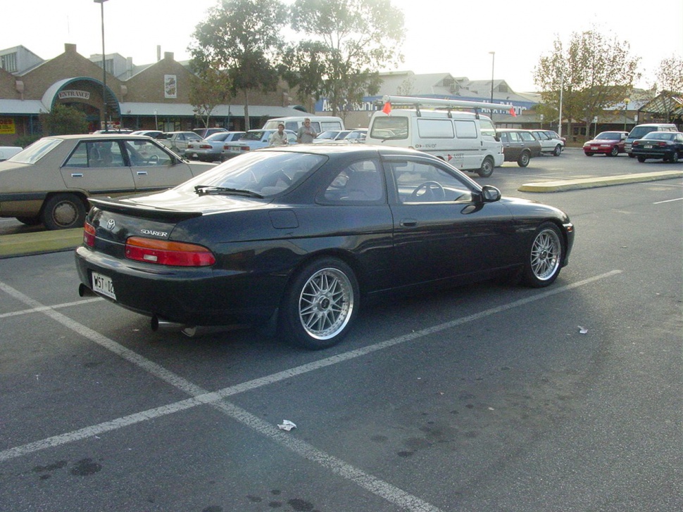 Rear side view of a black coupe with aftermarket wheels and spoiler