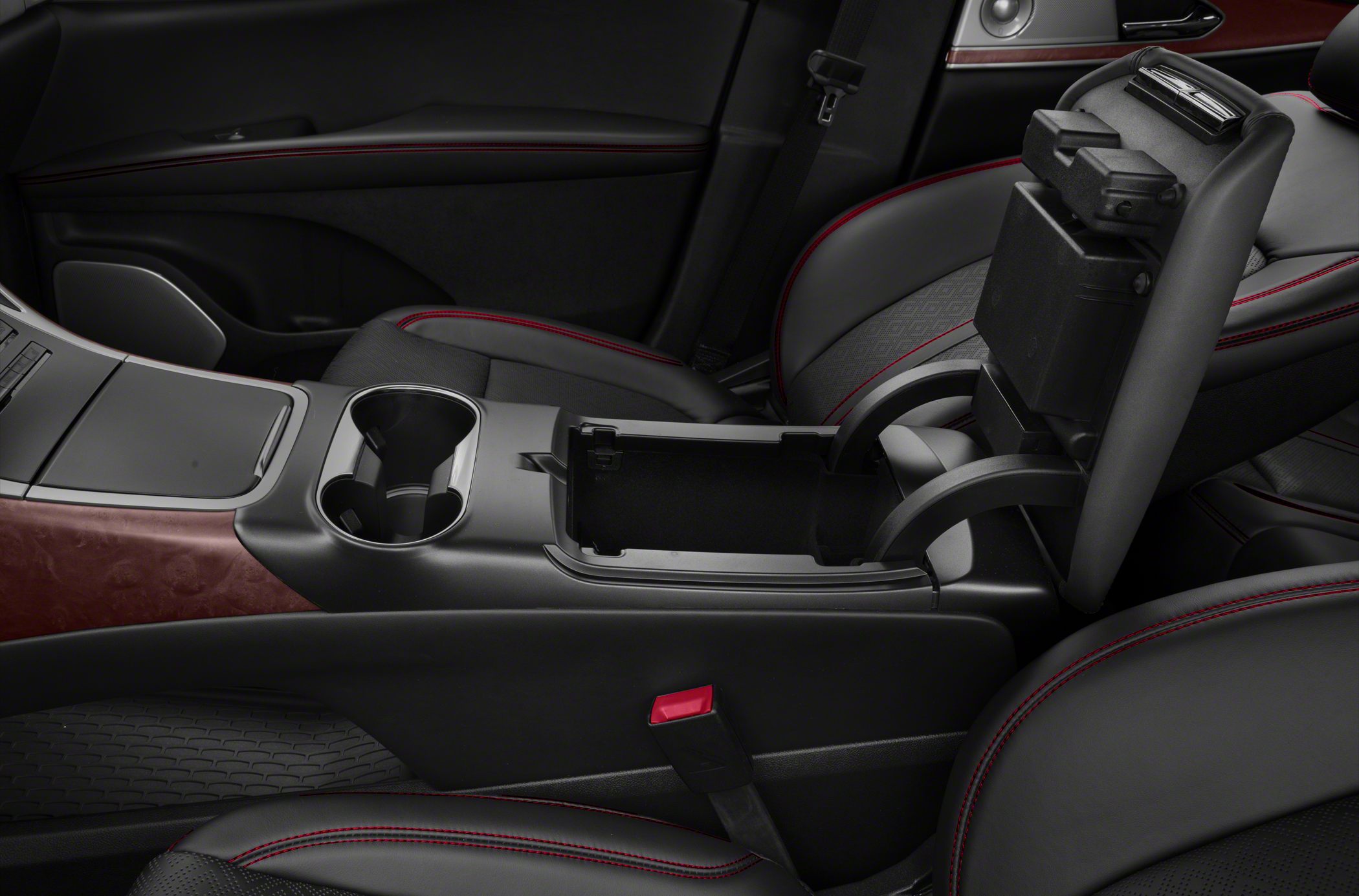 Center console with cup holders, open armrest storage, black leather seats, and red stitching