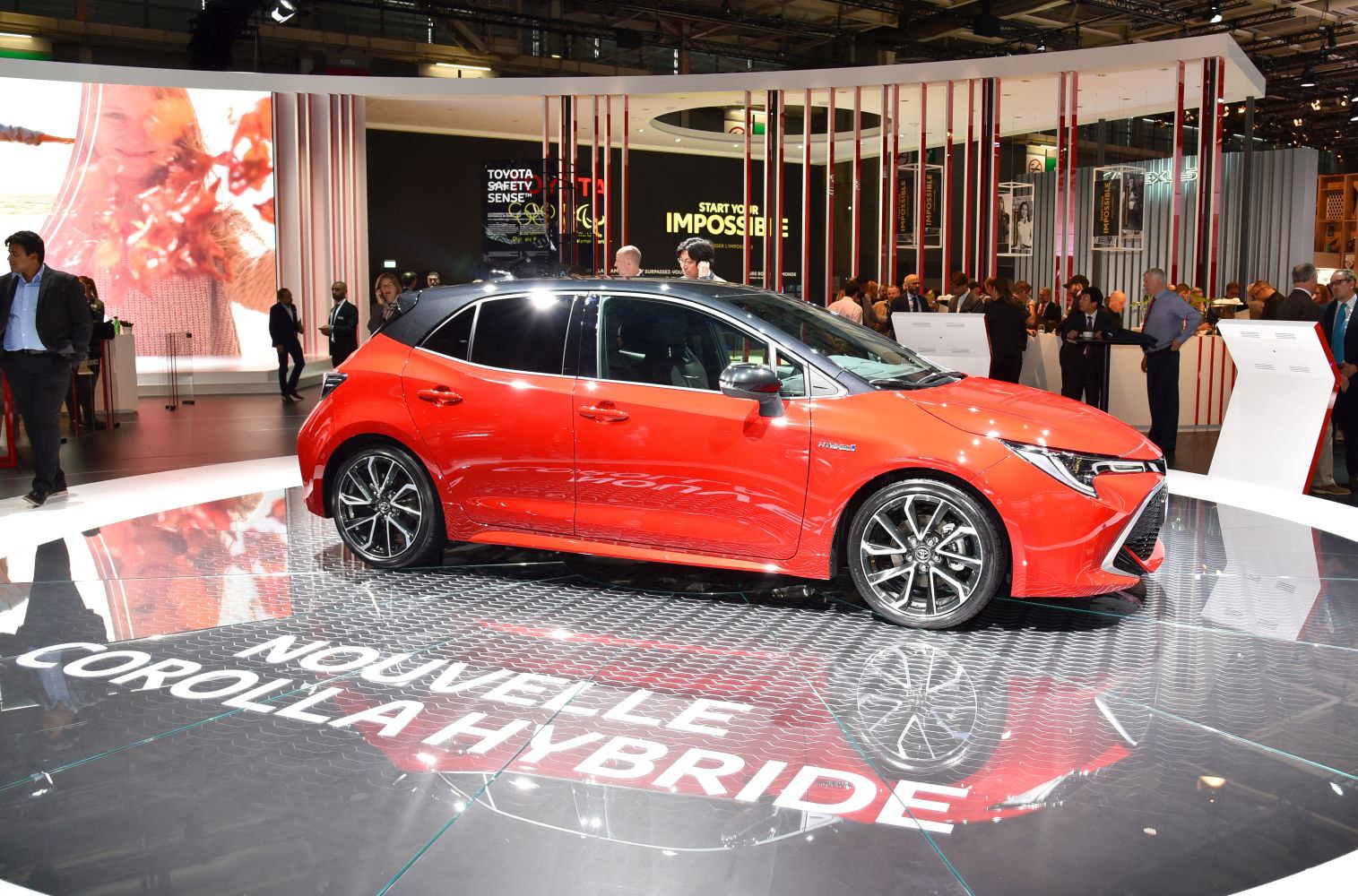 Red hybrid hatchback with black roof and alloy wheels, side profile view.
