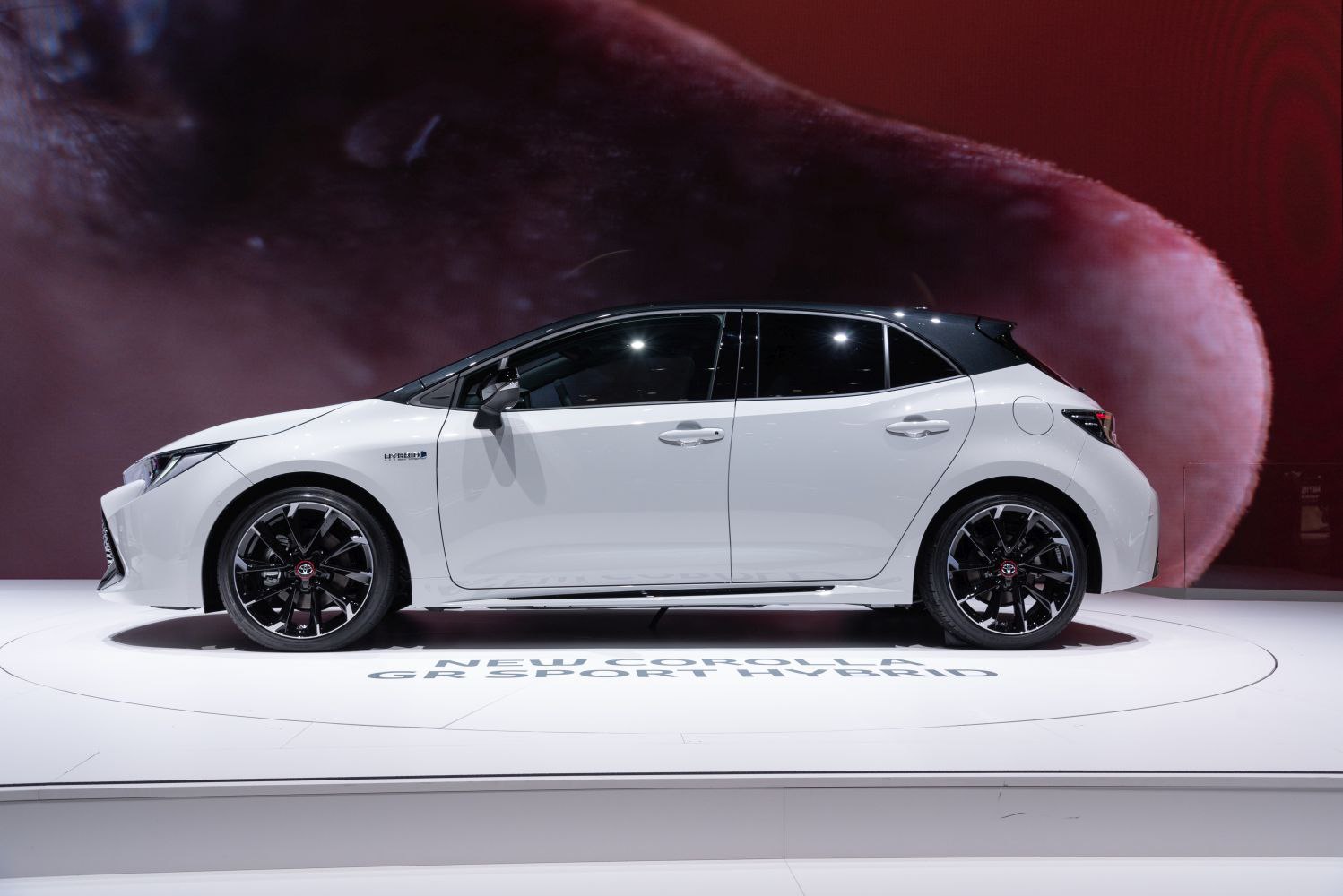 Side profile of a white hatchback with black alloy wheels and hybrid badge.