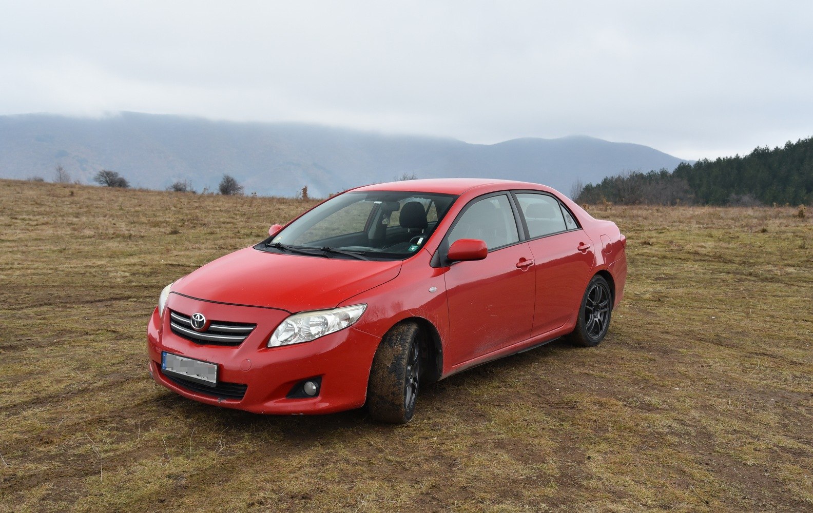 Red sedan front view with black alloy wheels on rough terrain