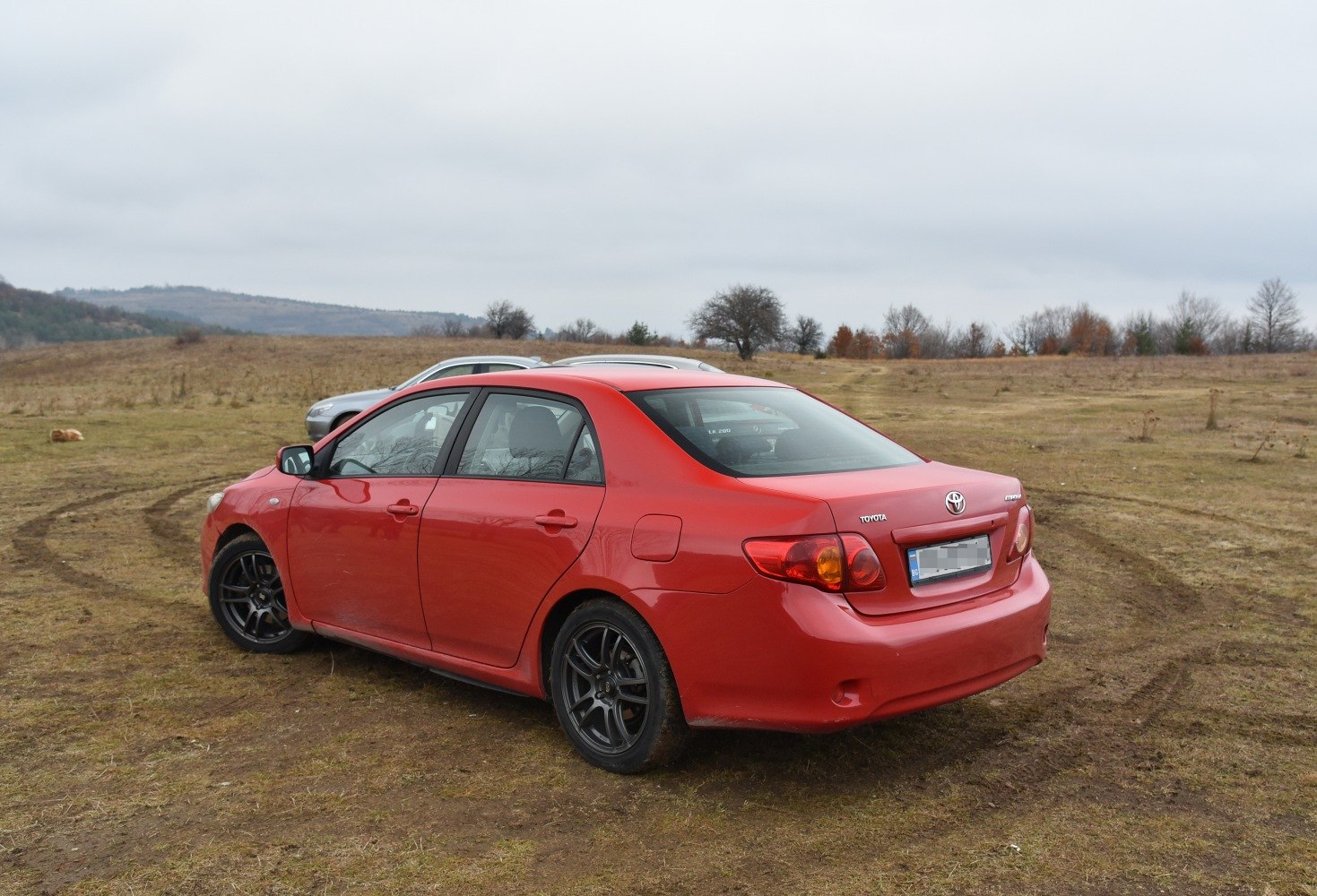 Red four-door sedan with black alloy wheels on grassy terrain