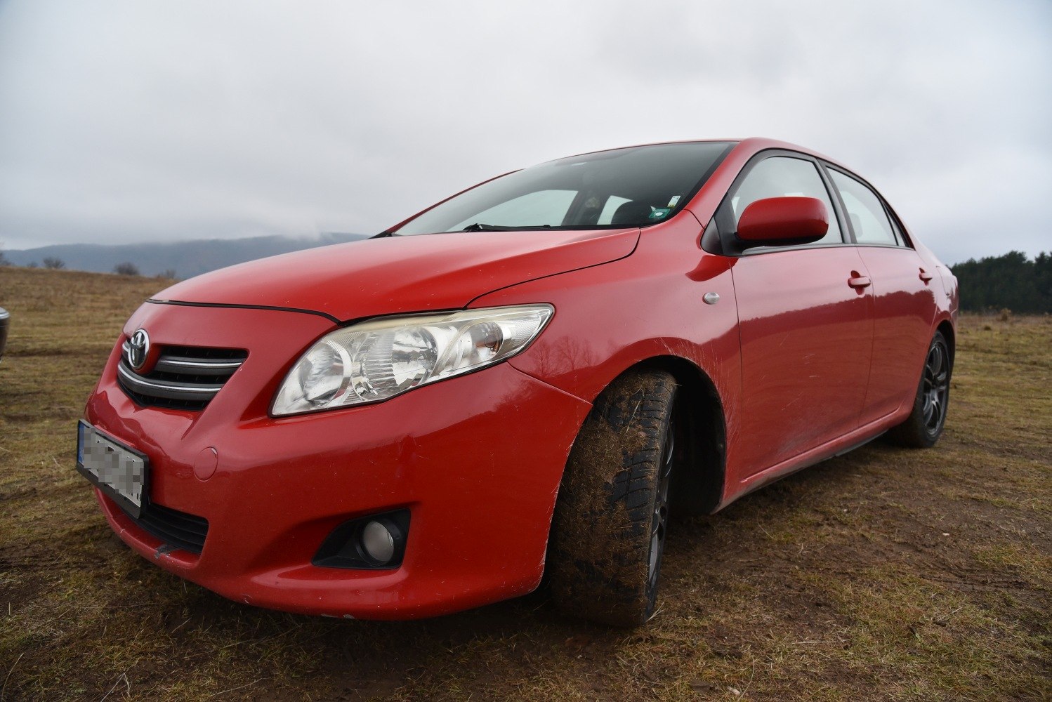 Red sedan front side with muddy tire on rough ground