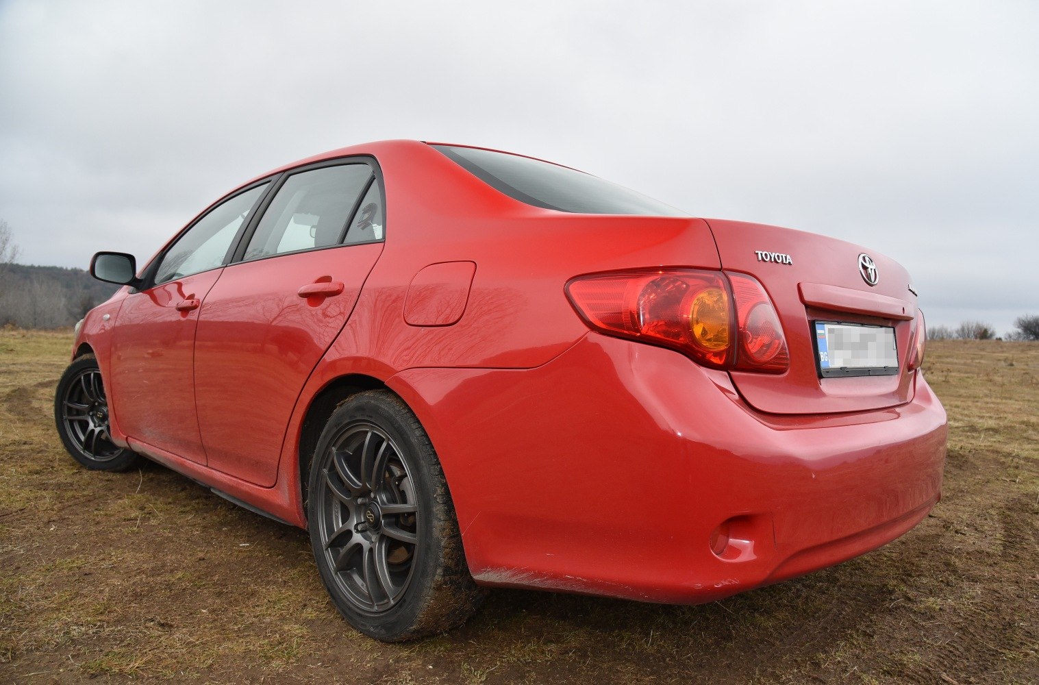 Rear and side view of a red sedan with alloy wheels on earthy ground