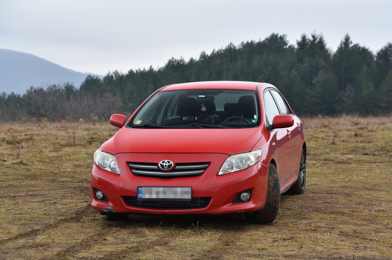 Red compact sedan front with grille and fog lights on earthy terrain