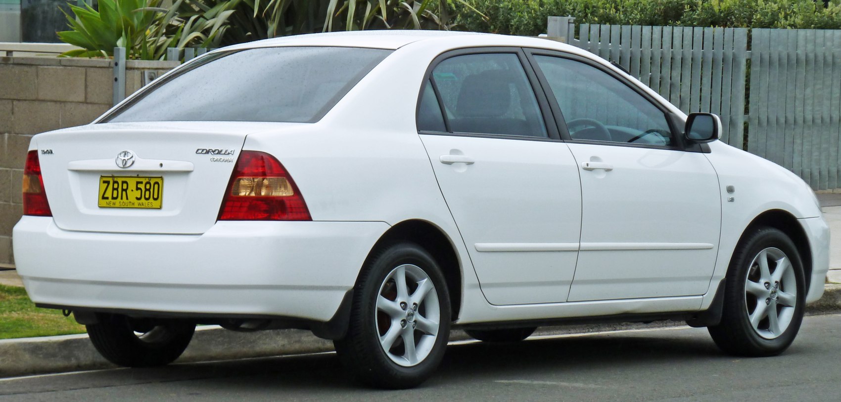 Rear side profile of a white sedan with alloy wheels and classic taillights.
