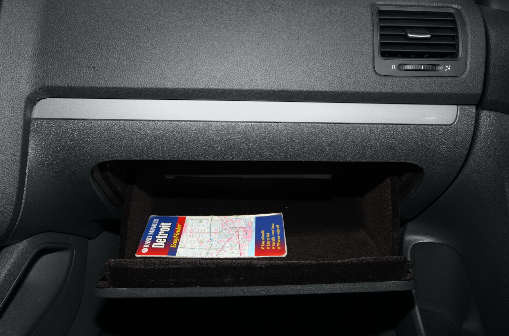 Open glove compartment with folded paper map inside car interior