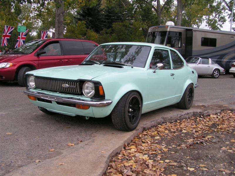 Side-angled front view of a classic compact coupe with round headlights and custom black wheels.