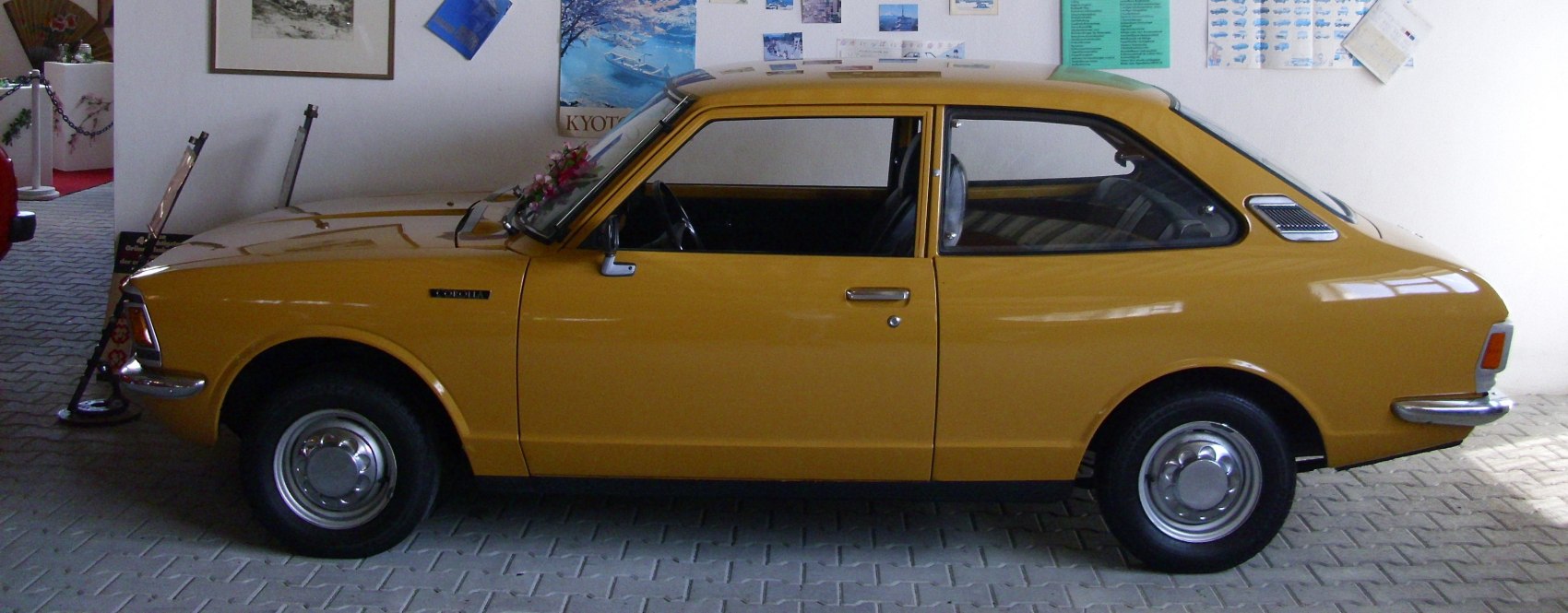 Yellow 2-door sedan with chrome hubcaps side profile