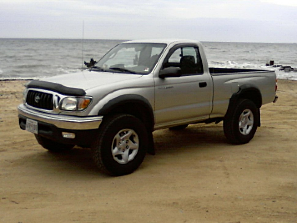 Silver single cab pickup truck on sandy beach near ocean