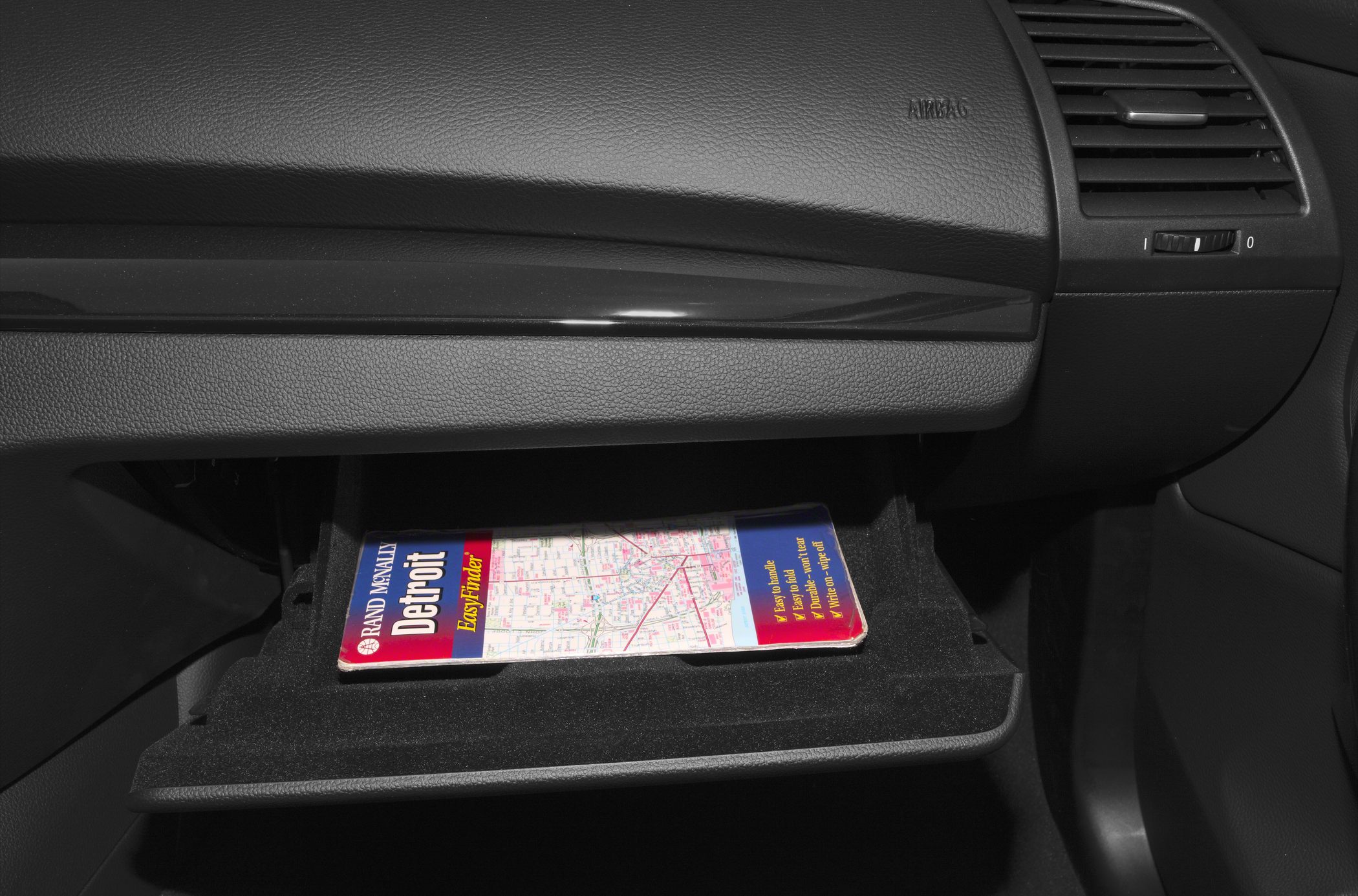 Open glovebox with a folded map inside and dashboard details
