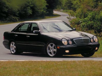 Black sedan with quad round headlights and five-spoke alloy wheels on road.