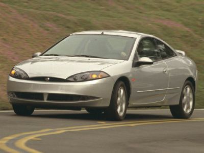 Silver two-door coupe with aerodynamic front and unique headlights rounding a bend
