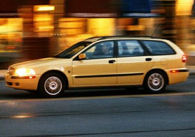 Side profile of a yellow station wagon with headlights on driving on street