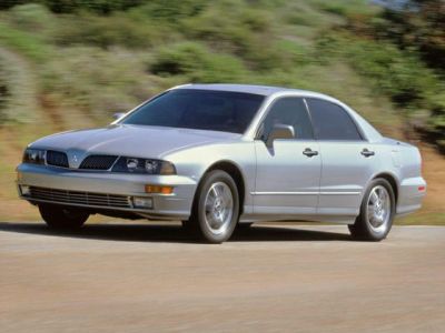 Silver four-door sedan driving on a road with front grille and alloy wheels