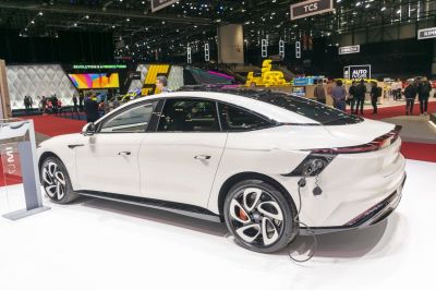 Electric sedan rear side view with charging cable connected and modern alloy wheels